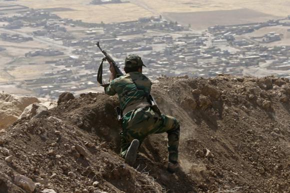 A Kurdish Peshmerga fighter moves into position while firing into ...